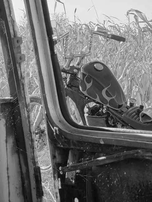 Chopper parked in a cornfield, framed by a rusted door